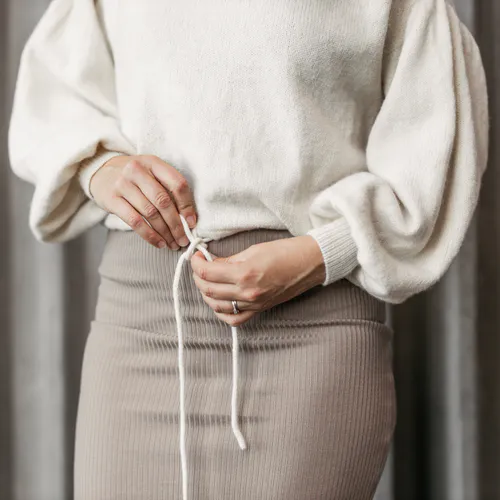 A woman wearing a cream jumper and her hands are tying the cord in the waist band into a bow
